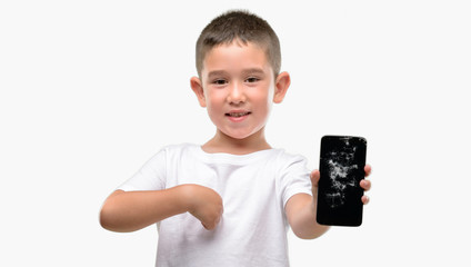 Dark haired little child holding broken smartphone with surprise face pointing finger to himself