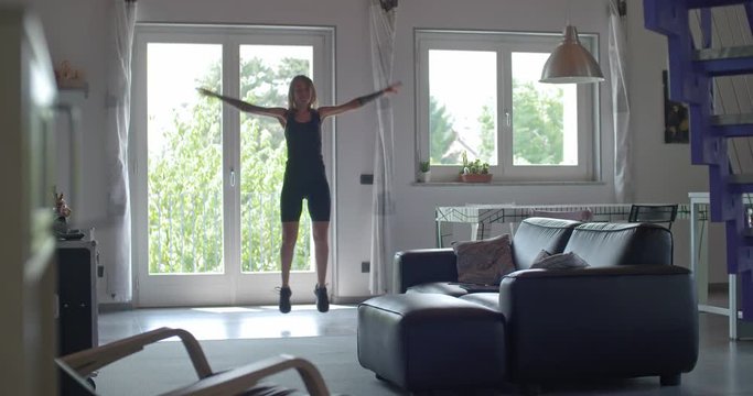 young tattooed woman doing jumping jacks exercise during home fitness sport workout .Living room domestic training. 4k slow motion video