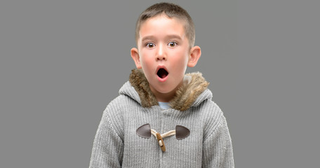 Dark haired little child wearing a coat scared in shock with a surprise face, afraid and excited...