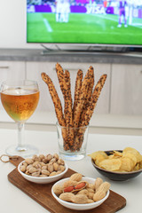 Football snacks with russian flag and football game on tv on the background Supporting national team concept Football fan food Beer, peanuts, pistacios, potato chips and tv remote control
