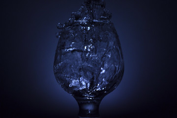 Simple still-life photo of whisky glass, water jet and dim colour light