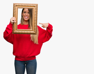 Beautiful young woman holding vintage frame very happy pointing with hand and finger