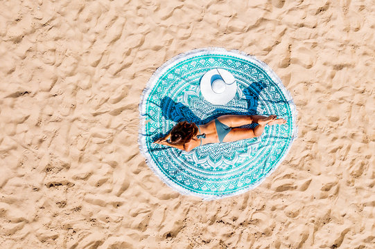 Top Aerial Drone View Of Woman In Swimsuit Bikini Relaxing And Sunbathing On Round Turquoise Beach Towel Near The Ocean