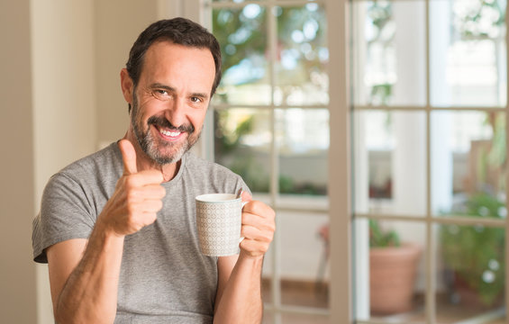 Middle age man drinking coffee in a cup happy with big smile doing ok sign, thumb up with fingers, excellent sign