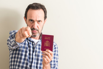 Senior man holding spanish passport pointing with finger to the camera and to you, hand sign,...