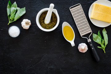 Cook homemade pesto sauce. Cheese, garlic, green basil, olive oil, salt near grater and mortar on black background top view copy space