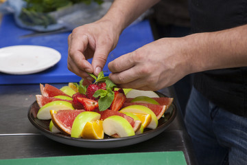 Hands of the cook, prepares a fruit salad