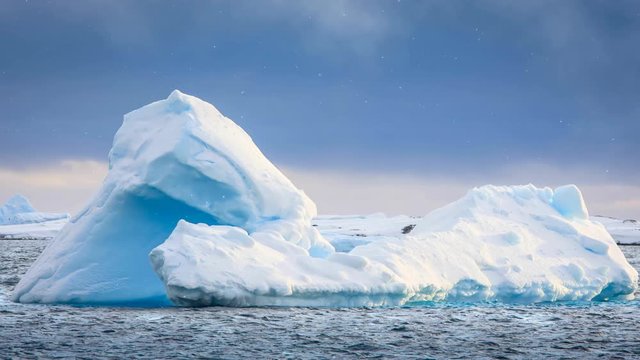 Antarctica glacier. Beautiful blue iceberg float in open ocean. Majestic winter landscape. Dramatic sky with snow fall in the background. Exploring, holiday, travel. 4K Slow Motion Time Lapse Parallax