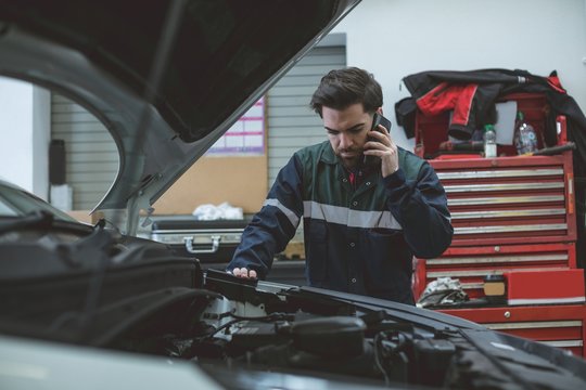 Mechanic talking on a mobile phone while examining car