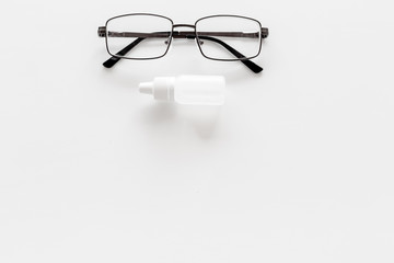 Eye drops in small bottle near glasses on white background top view copy space