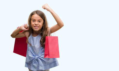 Brunette hispanic girl holding shopping bags annoyed and frustrated shouting with anger, crazy and yelling with raised hand, anger concept