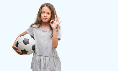 Brunette hispanic girl holding soccer football ball doing ok sign with fingers, excellent symbol