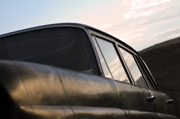Abandoned old black car. Close up. Soft focus. Front view from below of an old car. In the foreground the fender and behind the side with reflection of sky in car windows.