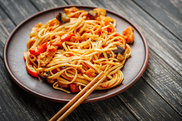 Udon stir fry noodles with meat and vegetables in sauce and chopsticks on black wooden background