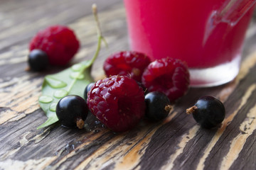 Still life with ripe berries of raspberries, black corn and a glass of juice in the background