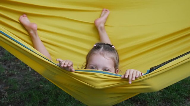 Girl child funny amuse enjoy lying in yellow hammock wagging barefooted legs