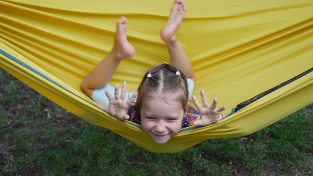 Girl child funny amuse enjoy lying in yellow hammock wagging barefooted legs smile