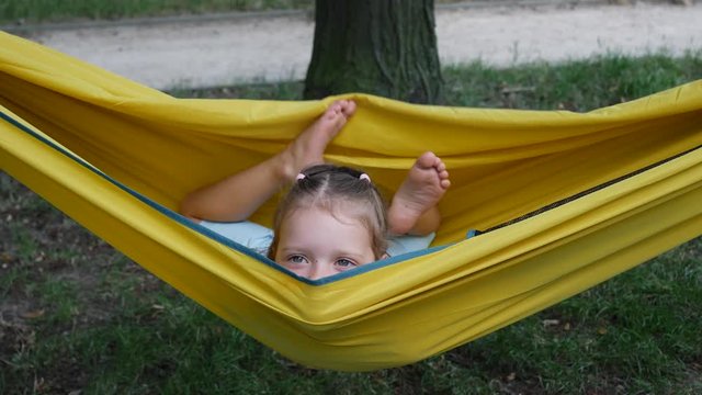 Girl child funny amuse enjoy lying in yellow hammock wagging barefooted legs