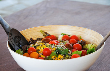 Fresh, healthy mixed salad bowl with lettuce, cherry tomatoes, corn and sunflower seeds on wooden table background. Vegetarian food. Wood cutlery set inside ready to serve