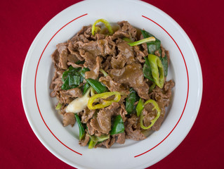 Top view of Mongolian beef on sauce with green chili peppers and vegetables on red background. Traditional Chinese non vegetarian dish