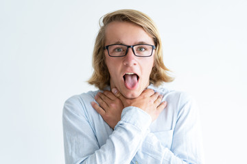 Portrait of young guy wearing glasses strangling himself. Caucasian student grimacing sticking out...