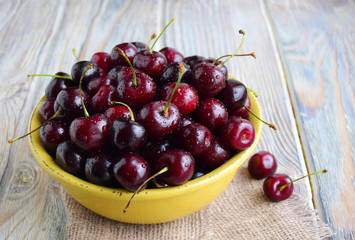 large berries of sweet cherry are in a yellow ceramic bowl. Close up, wooden background