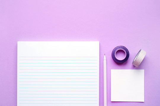 Beautiful office stationery flatlay with ruled notebook, pen, sticky note and paper clip on the bright desk with violet background.