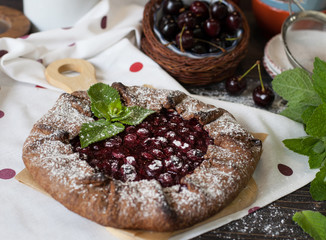 Сhocolate galette with cherries on brown wooden background. Summer pie.