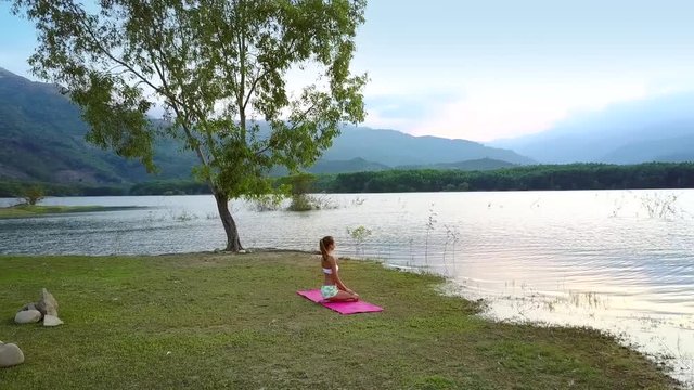 girl silhouette sits in yoga pose at tree watches lake hills