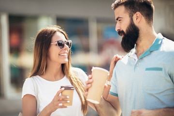 Smiling young couple  looking at each other while walking with coffee to go on street