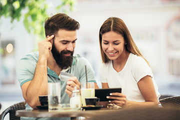 Beautiful couple having coffee on a date, using digital tablet and credit card for online shopping