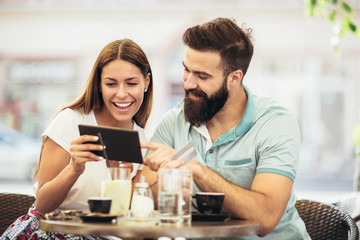 Beautiful couple having coffee on a date, using digital tablet and credit card for online shopping