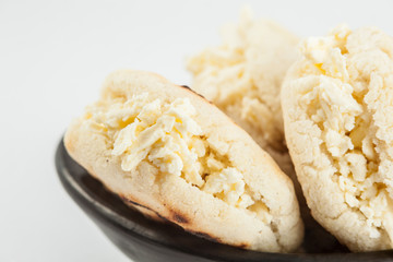 Colombian traditional white corn arepa stuffed with grated cheese in a black ceramic dish on black background