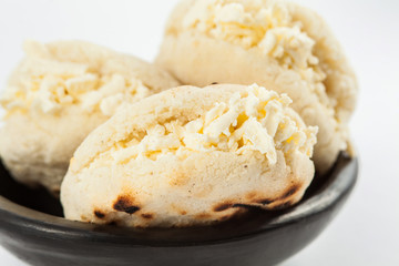 Colombian traditional white corn arepa stuffed with grated cheese in a black ceramic dish on black background