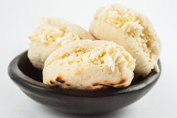 Colombian traditional white corn arepa stuffed with grated cheese in a black ceramic dish on black background