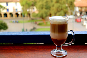 Hot cappuccino coffee in a transparent cup served at the terrace with blurred old town square of...
