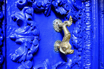 Vintage style dolphin shaped brass door knocker on vivid blue carved wood door, Cuzco, Peru  