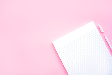 Beautiful office stationery flatlay with ruled notebook and white pen on the bright desk with pink background.