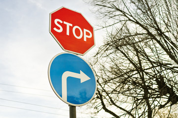 Stop sign and road sign turn to the right against a blue sky and a tree