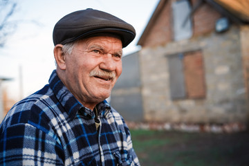 Happy smiling elder senior man portrait with a mustache in a cap on the background of a brick house...