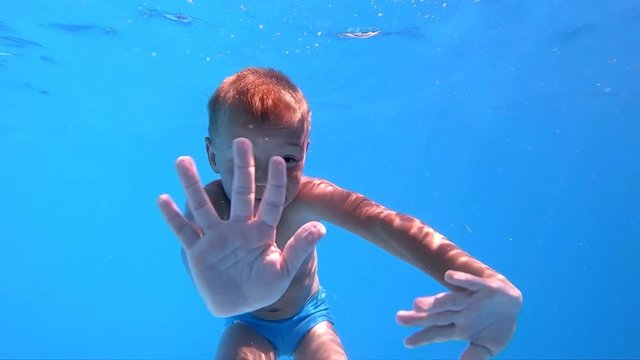 Children's games in the pool. Little, cute boy shows thumbs up under water. Slow motion.

