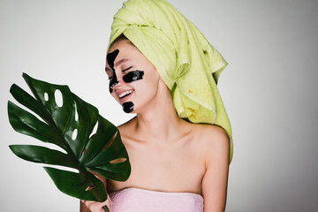 beautiful laughing girl with a green towel on her head applied a black cleansing mask on her face,...