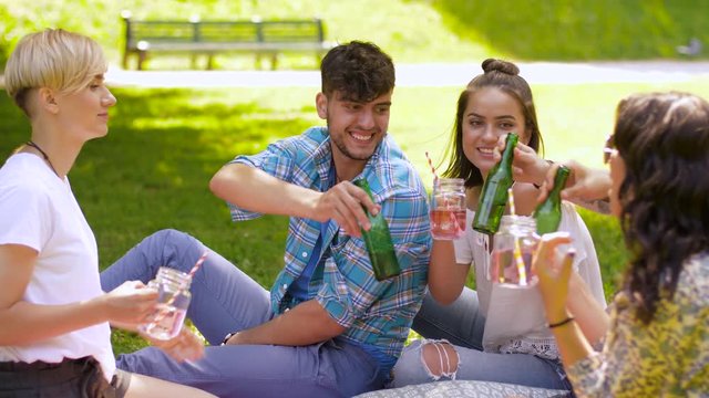 leisure, people and celebration concept - happy friends clinking non alcoholic drinks at summer park
