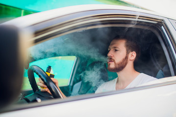 Man vaping e-cigarette with e-liquid, close-up, breathes out large cloud of steam or vapor. Vape...