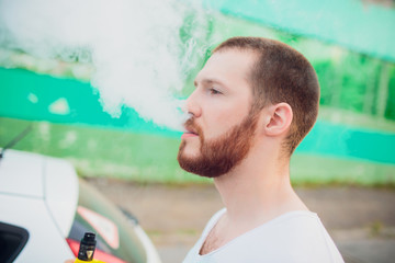 Man vaping e-cigarette with e-liquid, close-up, breathes out large cloud of steam or vapor. Vape...