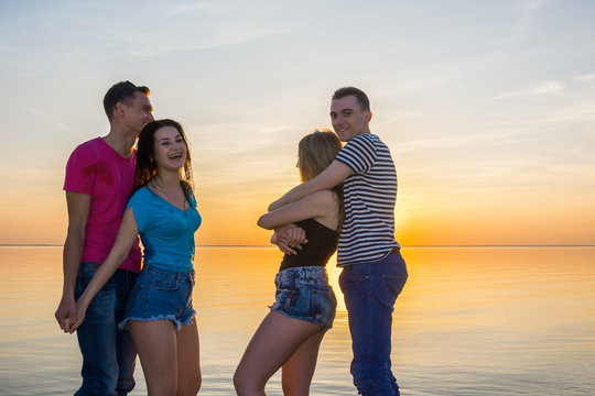 Young people, guys and girls are embrace in front of a sea at sunset