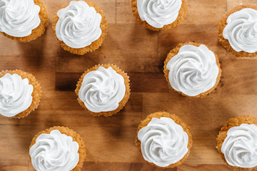 Cupcakes and muffins with delicate whipped cream stand on wooden plank on, top view flat lay