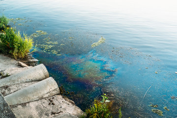 Sewer pipes at shore, stain of oil or fuel on water surface, nature pollution by toxic chemicals, dirty sea