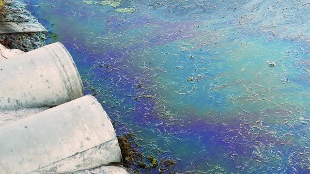 Sewer pipes at shore, stain of oil or fuel on water surface, nature pollution by toxic chemicals, dirty sea concept