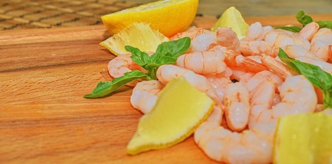 Cooked and peeled prawns with slices of lemon and leaves of basil on chopping board. Food photography. Healthy food. Bio recipe. Copy space